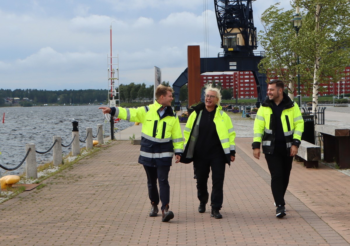 Tre personer går på en kaj med gula jackor