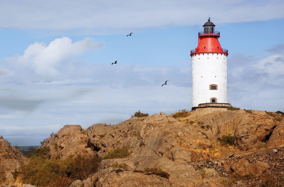 Landsorts fyr med klippa i förgrunden och blå himmel med moln i bakgrunden.