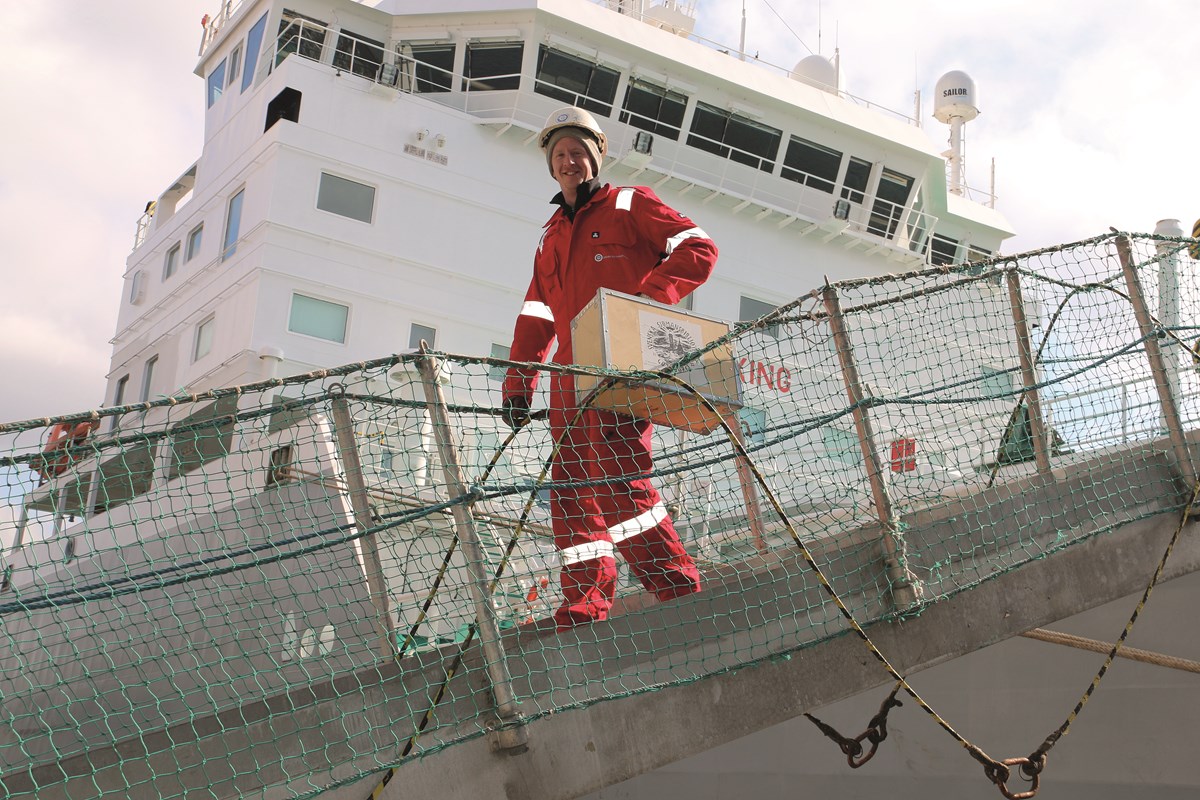 Besättningsman på väg med en låda underhållning. Från tidigare tillfälle. Foto: Glenn Hjelle Person med trälåda på väg mot fartyg.