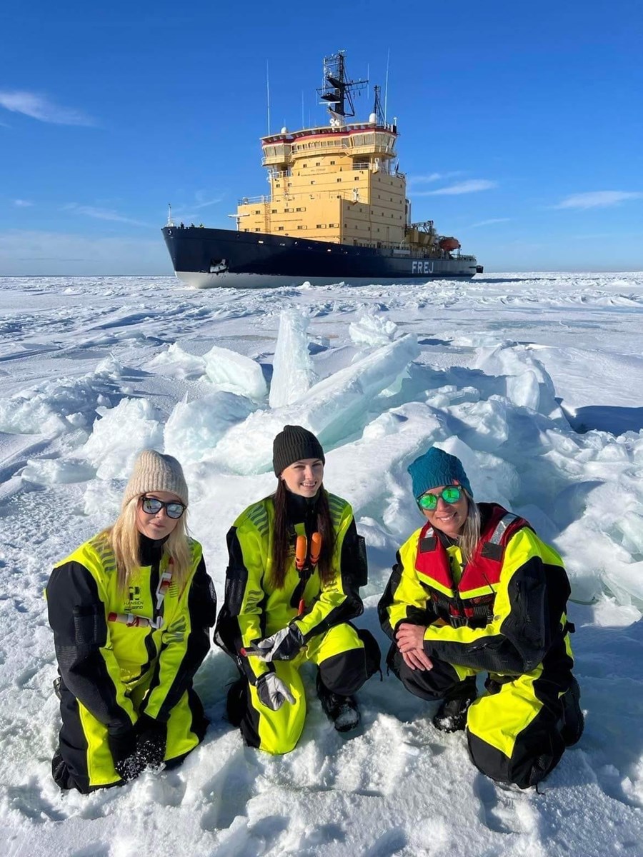 Från vänster: Maja Näslund, Malva Jungquist & Mimmi Backman stoltserar med Frej i fjärran. Bild på tjejer som sitter framför en isbrytare