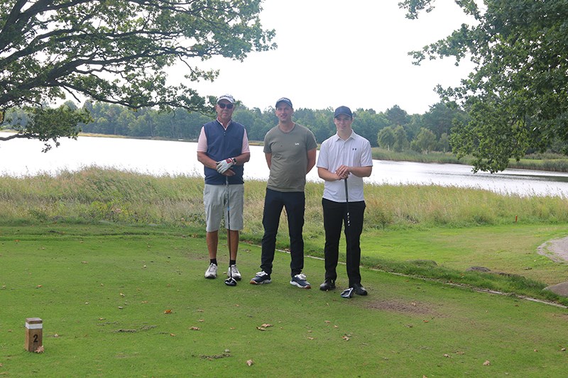 Tre golfspelare står på golfbana, med vatten i bakgrunden