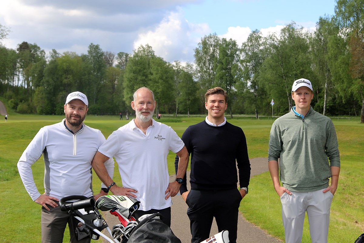 Fyra golfare med golfbanan och trädlinjen i bakgrunden